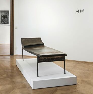 An exhibition featuring a metal lounger, a black-and-white picture in the backgr